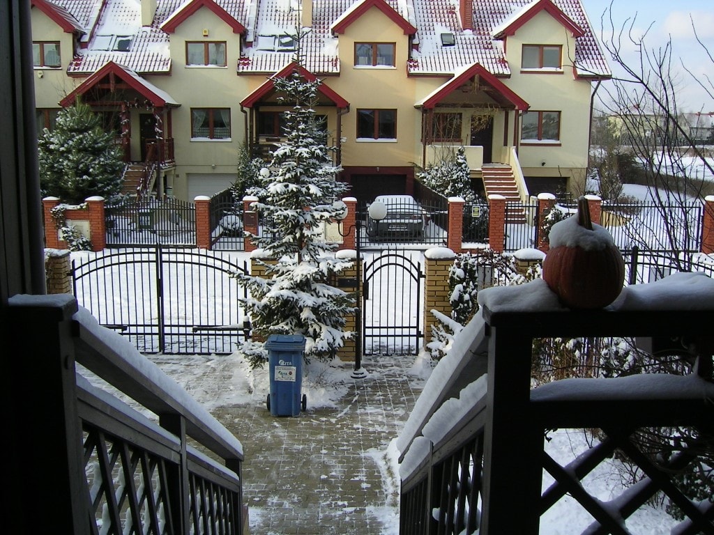 zdjęcie przedstawiające zaśnieżoną ulicę i ogrodzenie przed domem
