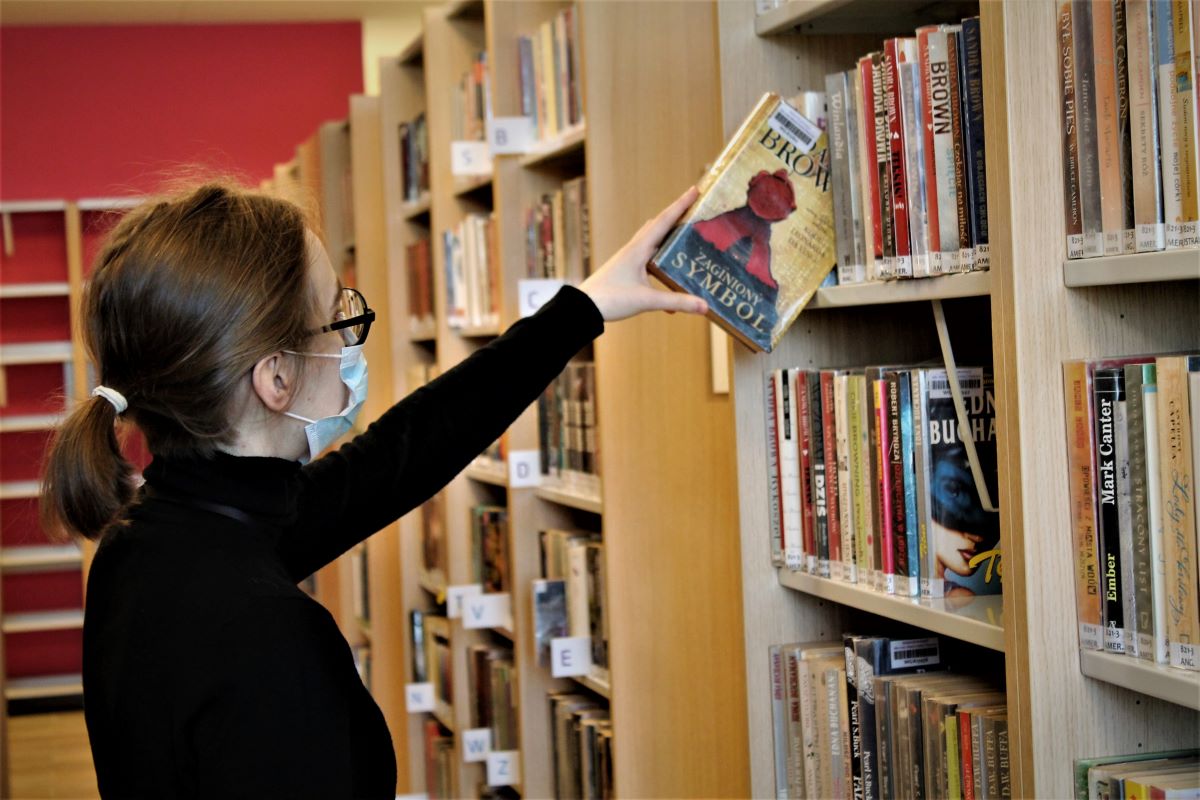 Osoba wybiera książkę w bibliotece
