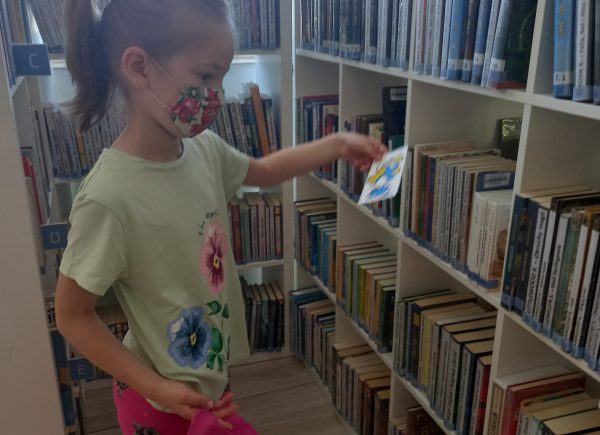 Dziewczynka poszukuje między półkami wydrukowanych ilustracji smerfów