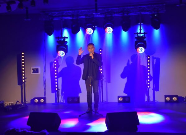 Robert Moskwa stoi na scenie. Mężczyzna śpiewa. W tle niebieskie światła.