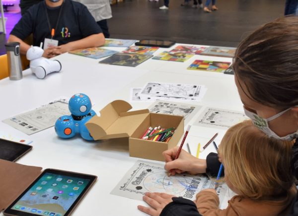 Dzieci kolorują kolorowanki. Na stole leżą flamastry, tablet i robot edukacyjny.