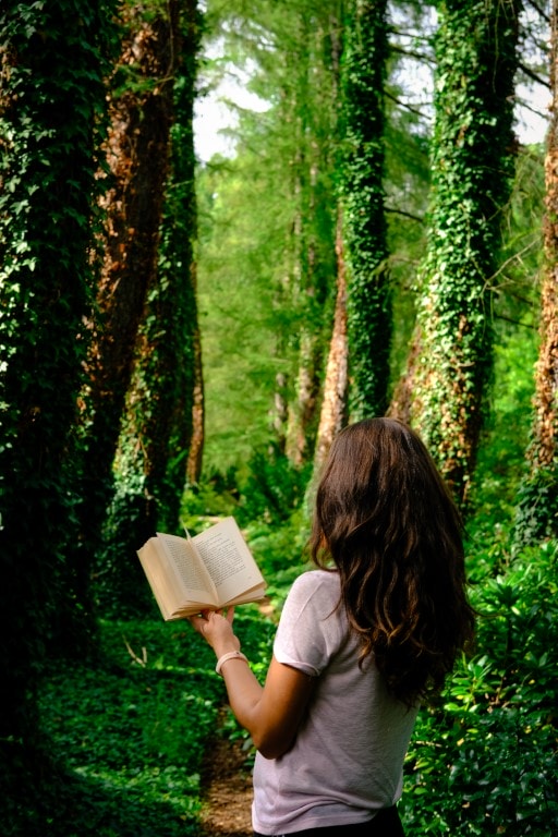 Na zdjęciu dziewczynka czytająca książkę w lesie.