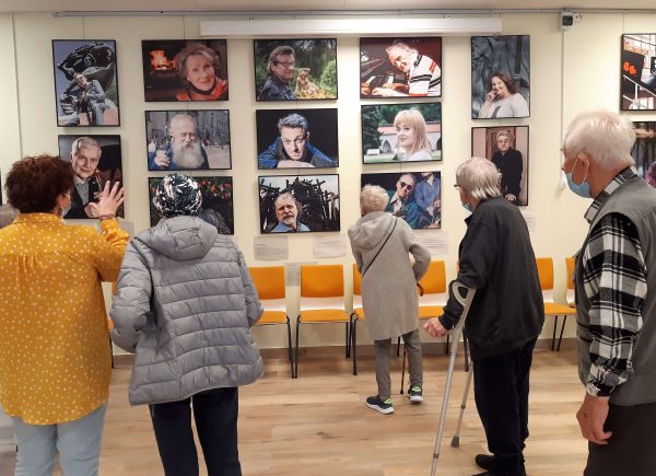 Zdjęcie przedstawia mieszkańców domu seniora "Rezydencja Orpea" i Sylwię Chojnacką Tuzimek. Seniorzy oglądają wystawę "Sztukmistrzowie" Macieja Kłosia.