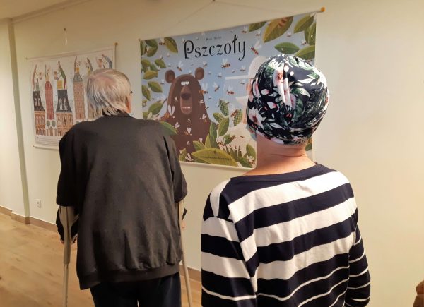 Zdjęcie przedstawia mieszkańców domu seniora "Rezydencja Orpea". Seniorzy oglądają wystawę "Pszczoły".