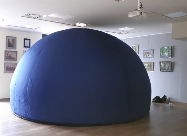 Zdjęcie przedstawia rozstawione w sali przenośne dmuchane niebieskie planetarium, sala jest pomalowana na biało i ozdobiona galerią obrazów