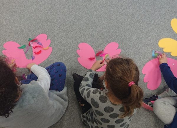 Dziewczynki ozdabiają kolorowe skrzydełka z papieru kolorowymi piórkami