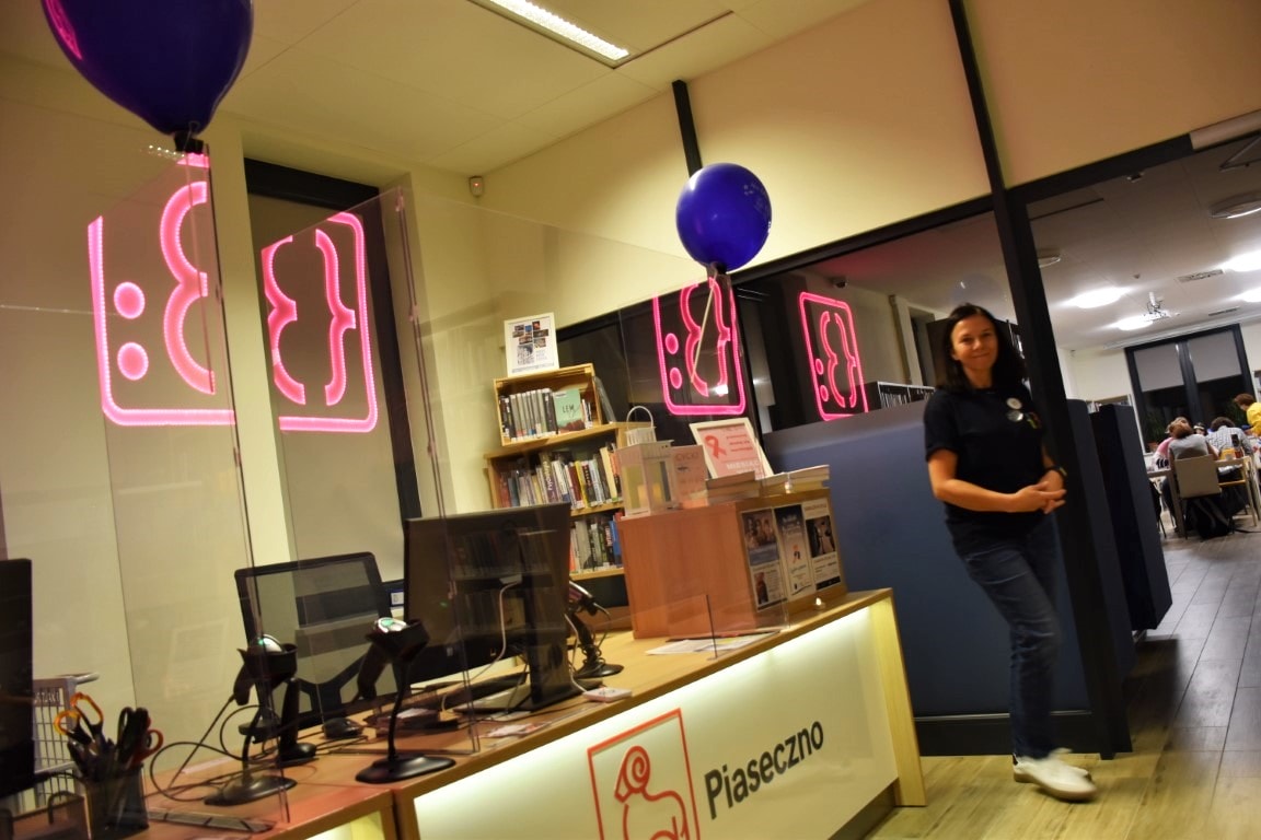 Na zdjęciu widać biurka znajdujące się w oddziale dla dorosłych, balony i logo biblioteki. Po prawej stronie można dostrzec organizatorkę wydarzenia.