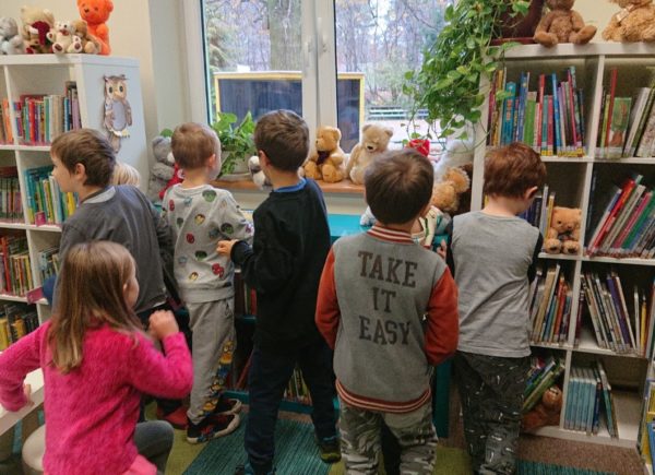 Dzieci oglądają wystawę misiów pluszowych. Są rozbiegane, dotykają grzbiety książek i sięgają po misie