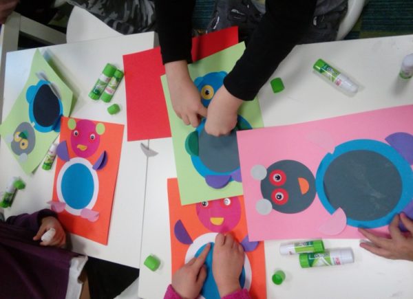 Kolorowe kartki ozdobione kolorowymi kółkami - dzieci pracują nad wyklejanką w kształcie misia