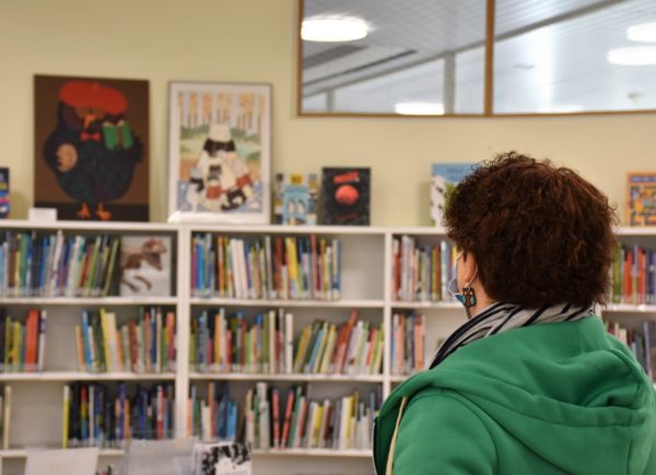 Zdjęcie przedstawia uczestniczkę projektu. Kobieta ogląda regały z książkami w bibliotece w Töölö.
