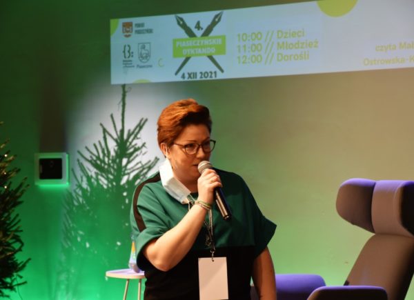 Wicedyrektor Biblioteki Głównej Sylwia Chojnacka-Tuzimek stoi na scenie i trzyma w ręku mikrofon.