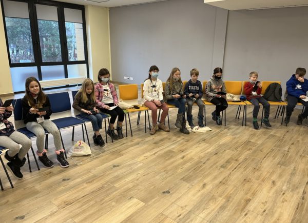 Zdjęcie przedstawia grupę słuchaczy Piaseczyńskiego Uniwersytetu Dziecięcego mają zamknięte oczy i zapoznają się z wypukłymi piktogramami i Alfabetem Braille’a