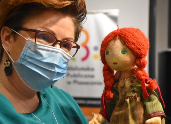 Wicedyrektor Biblioteki Głównej Sylwia Chojnacka-Tuzimek trzyma w ręku lalkę przypominającą Aliaszkę. Kobieta pozuje do zdjęcia.