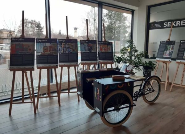 Plansze wystawy dwujęzycznej „Podróże po literaturze”. Przed nimi stoi rower bookcrossingowy.