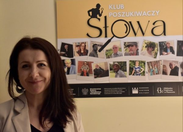 Joanna Miter na tle planszy rozpoczynającej wystawę Klubu Poszukiwaczy Słowa