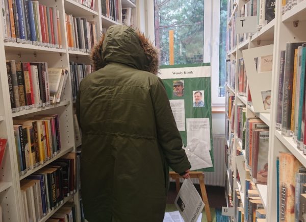 Czytelniczka ogląda tablicę wystawową umieszczoną miedzy regałami z książkami