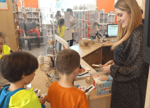 Dzieci podają bibliotekarce papierowe zegarki