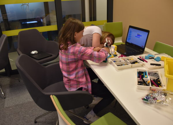 Dziewczynka siedzi przed komputerem i buduje z klockó LEGO