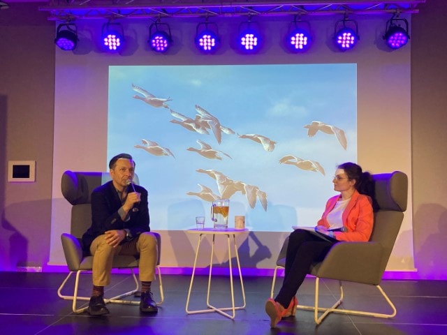 Jacek Karczewski z prowadzącą wywiad na scenie, w tle prezentacja zdjęć ptaków