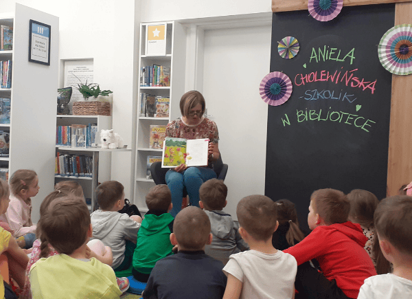 Aniela Cholewińska-Szkolink trzyma w ręku książkę. Dzieci słuchają autorki.