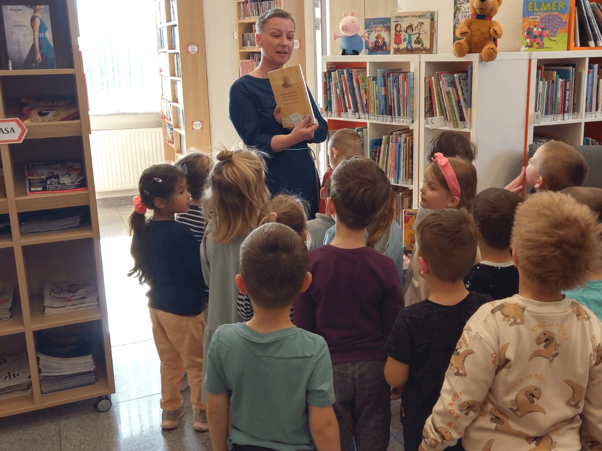 Bibliotekarka pokazuje dzieciom księgozbiór