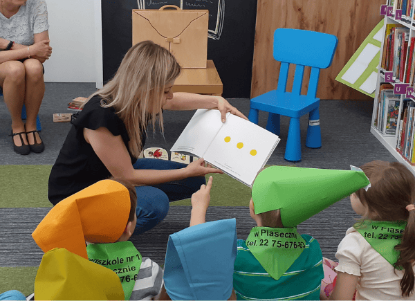 Bibliotekarka czyta wspólnie z dziećmi książkę "Naciśnij mnie"
