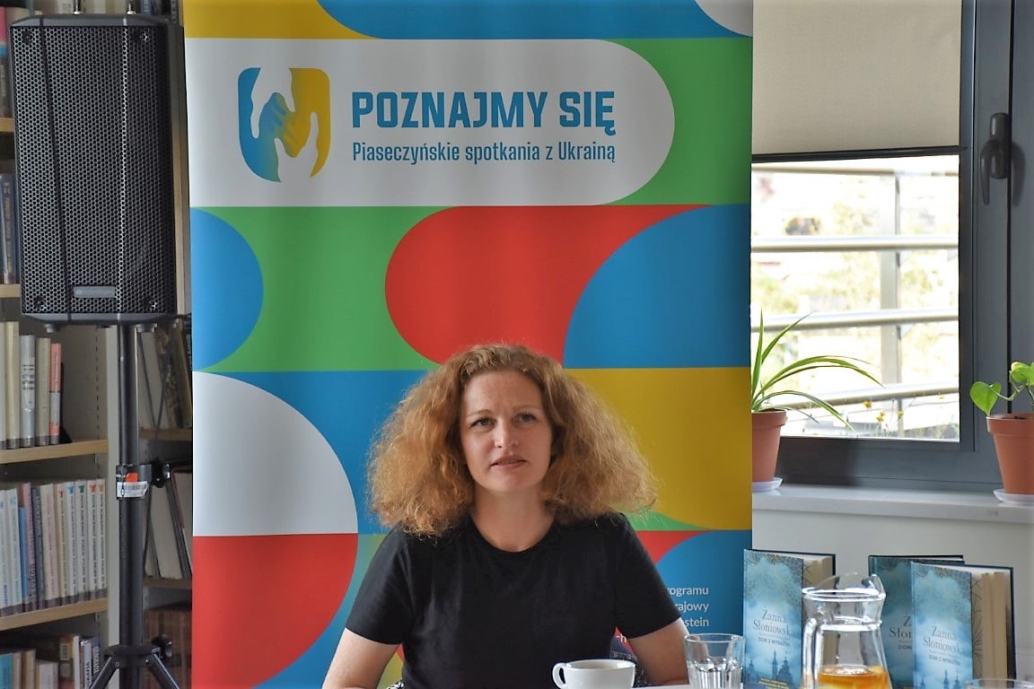 Żanna Słoniowska na tle baneru projektu "Poznajmy się - Piaseczyńskie spotkania z Ukrainą".