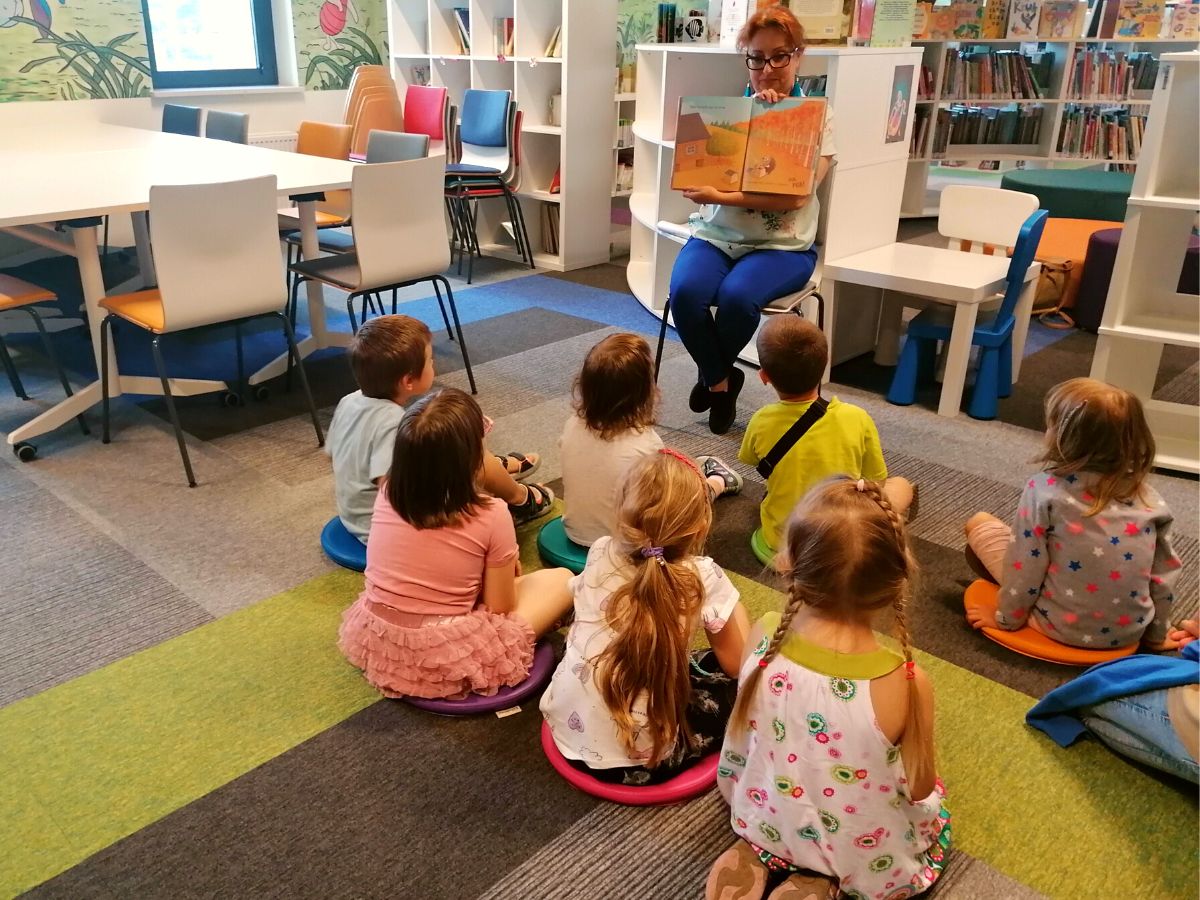 Bibliotekarka czyta dzieciom książeczkę “Jak dobrze mieć sąsiadów”