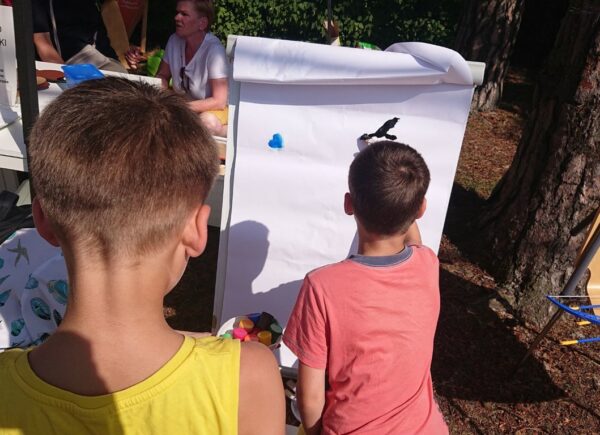 Dwóch chłopców ozdabia pieczątkami i farbami białą kartkę papieru