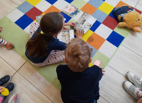 Dzieci siedzą na dywanie i oglądają papierowe obrazki