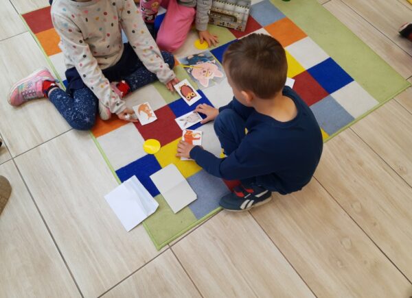 Dzieci siedzą na dywanie i oglądają papierowe obrazki