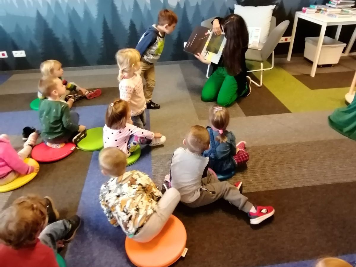 Bibliotekarka pokazuje przedszkolakom książeczkę ruchomą