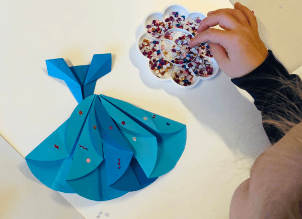 Dziewczynka ozdabia sukienkę wykonaną metodą origami