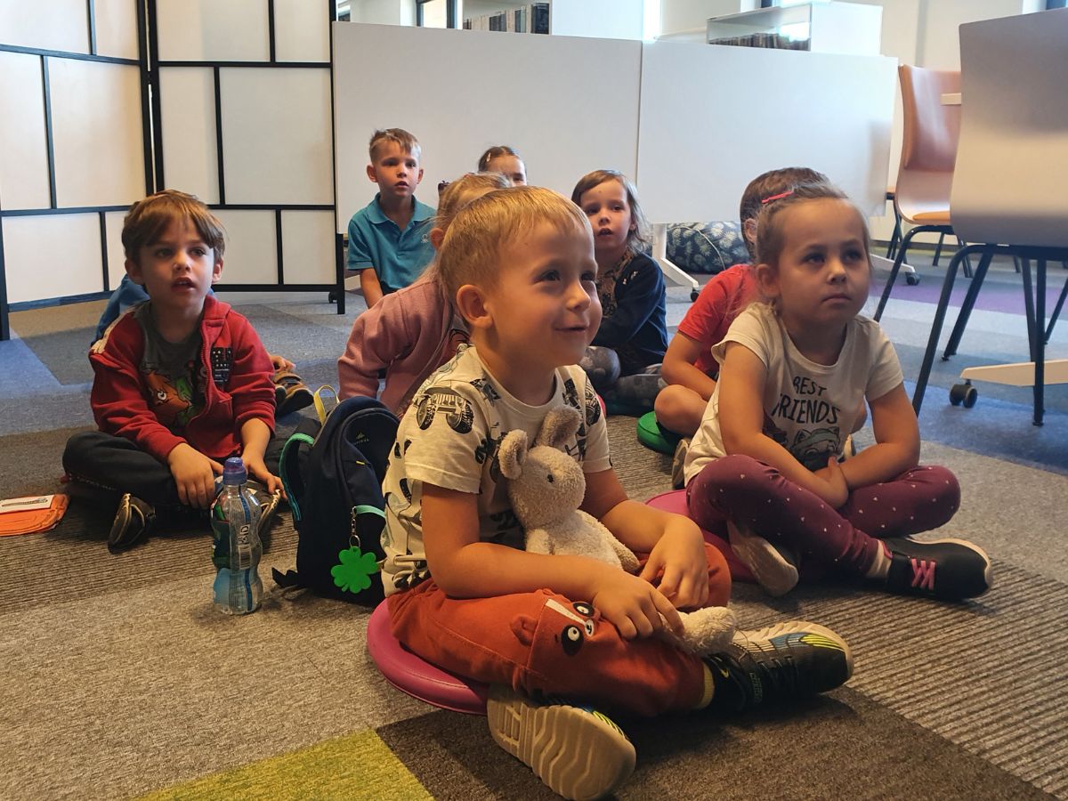 Dzieci z zaciekawieniem słuchają opowieści czytanej przez Panią bibliotekarkę