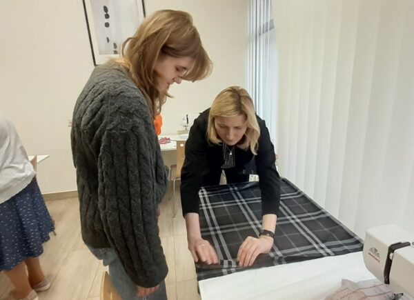 Prowadząca Małgorzata Goławska instruuje uczestniczkę jak dobrze przygotować materiał do szycia