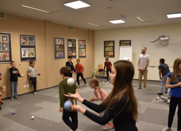 Grupa dzieci podrzuca kolorowe piłeczki ćwicząc żonglowanie