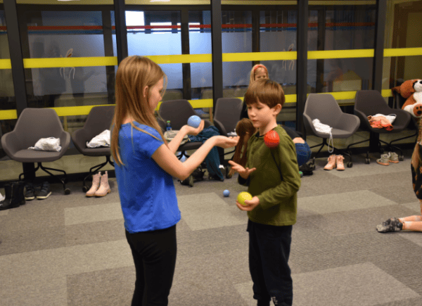 Dwoje dzieci podrzuca kolorowe piłeczki ćwicząc żonglowanie