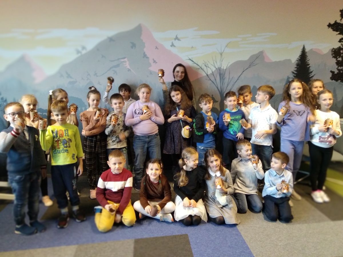 Uczniowie wraz z Panią bibliotekarką pozują do współnego zdjęcia. Dzieci trzymają w rękach wykonane jeże.