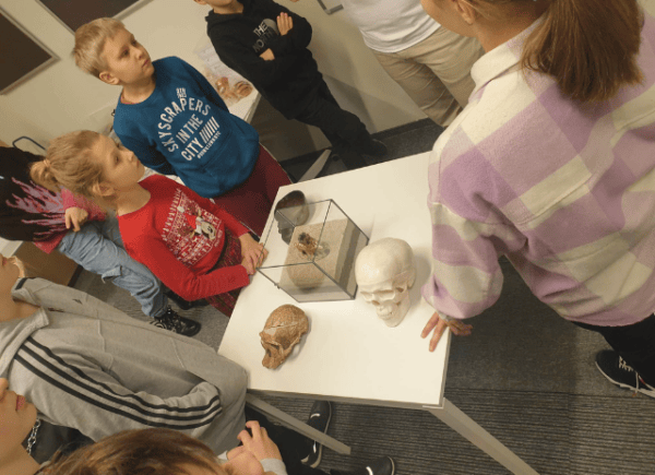 Dzieci słuchają prowadząceg i oglądają prezentowane przedmioty - czaszkę oraz warstwy ziemi