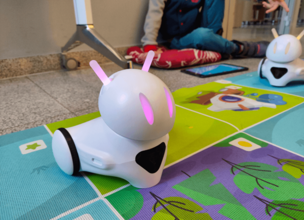 Robot Photon na macie edukacyjnej, na drugim planie dziecko programuje drugiego robota