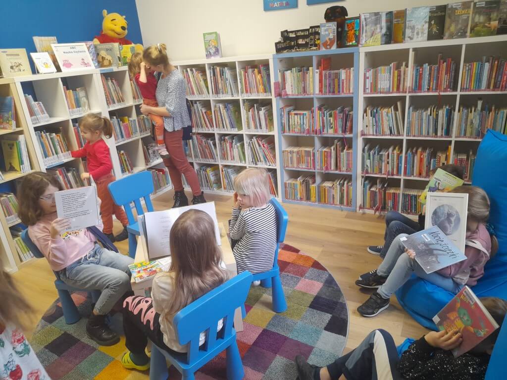 Dzieci siedzą przy stolikach i oglądają książki