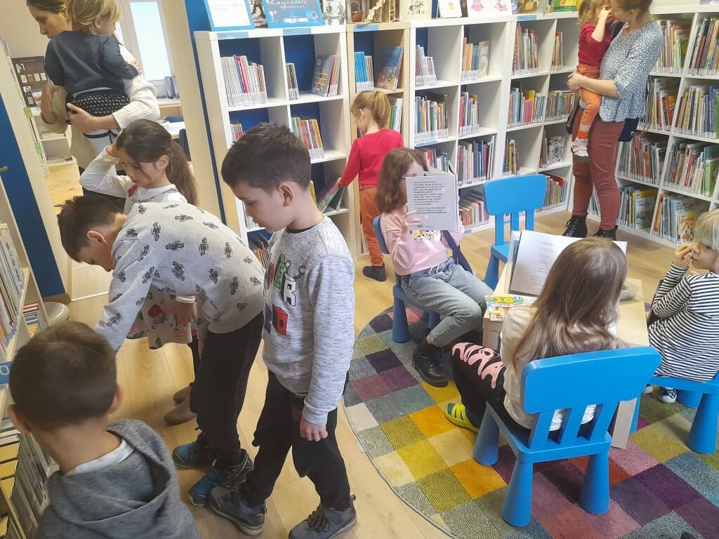 Dzieci siedzą przy stolikach i oglądają książki