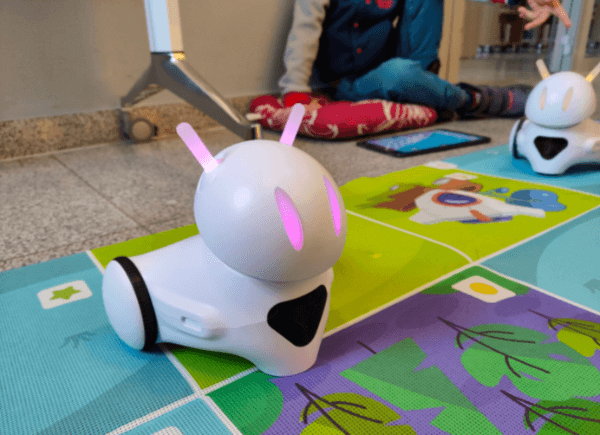 Robot Photon na macie edukacyjnej, na dalszym planie dziecko programuje drugiego robota