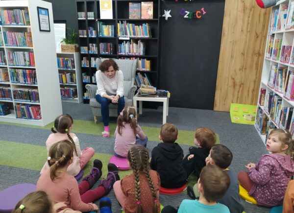 Dzieci siedzą na dywanie i słuchają bibliotekarki