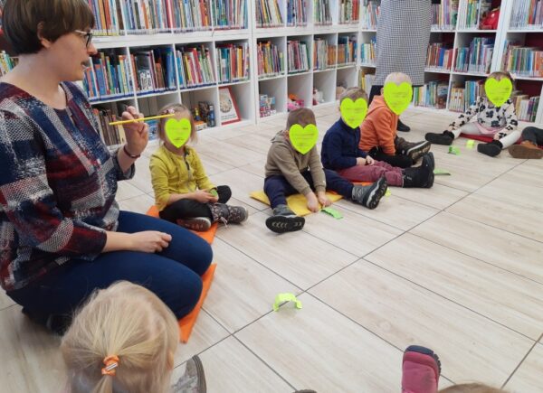 Dzieci siedzą na podłodze, pani bibliotekarka opowiada