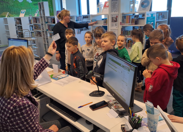 Dzieci zwiedzające bibliotekę dowiadują się jak można się zapisać do biblioteki.