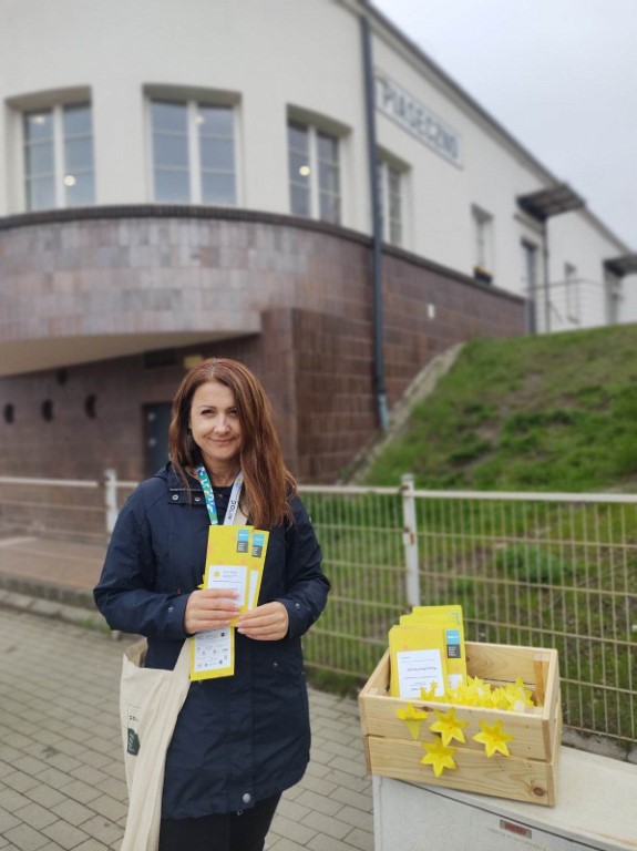 wolontariuszka przed dworcem PKP w Piasecznie rozdaje papierowe żonkile