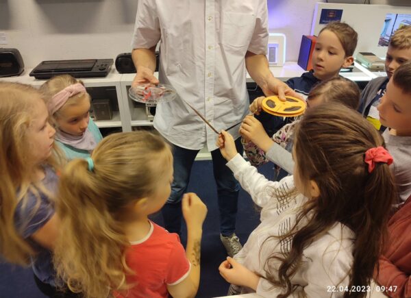 Prowadzący pokazuje dzieciom taśmę magnetofonową na szpuli
