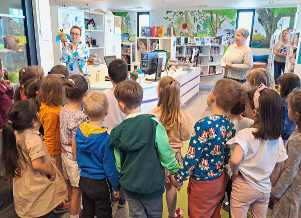 Panie bibliotekarki prezentuja dzieciom prace plastyczne wykonywane podczas zajęć odbywających się w bibliotece