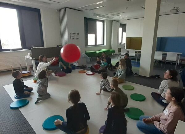 Uczestnicy warsztatów siedzą na podłodze i odbijają do siebie olbrzmi balon